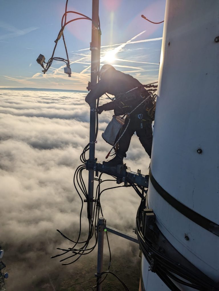 Industriekletterer bei der Arbeit an einem Mobilfunkmast über den Wolken